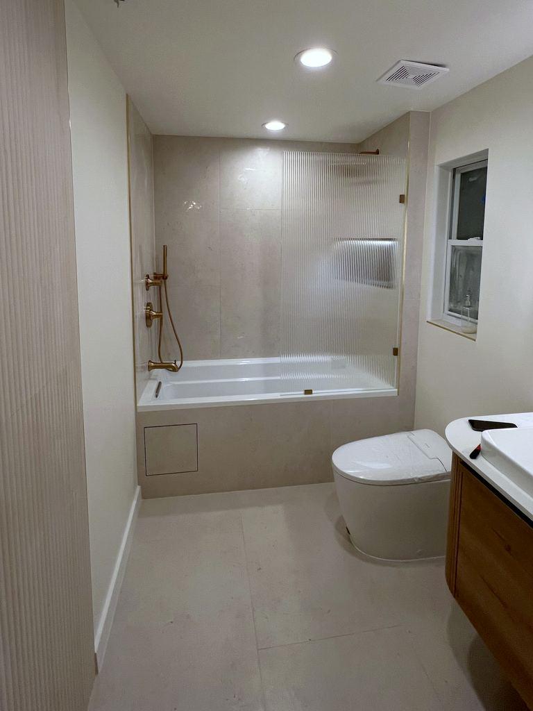 The same bathroom after the remodel: large-format stone tile, a new tub, brass fixtures and a fluted glass panel