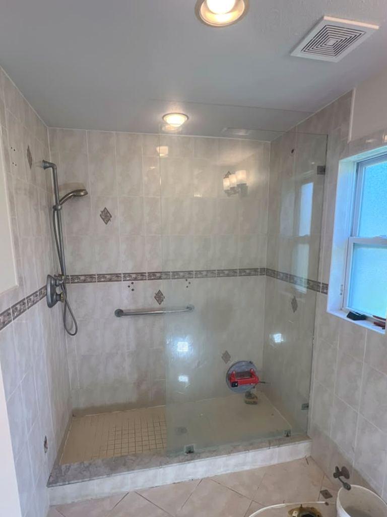 Bathroom before the remodel: dated beige tile with a decorative border, a grab bar and a step-over shower curb