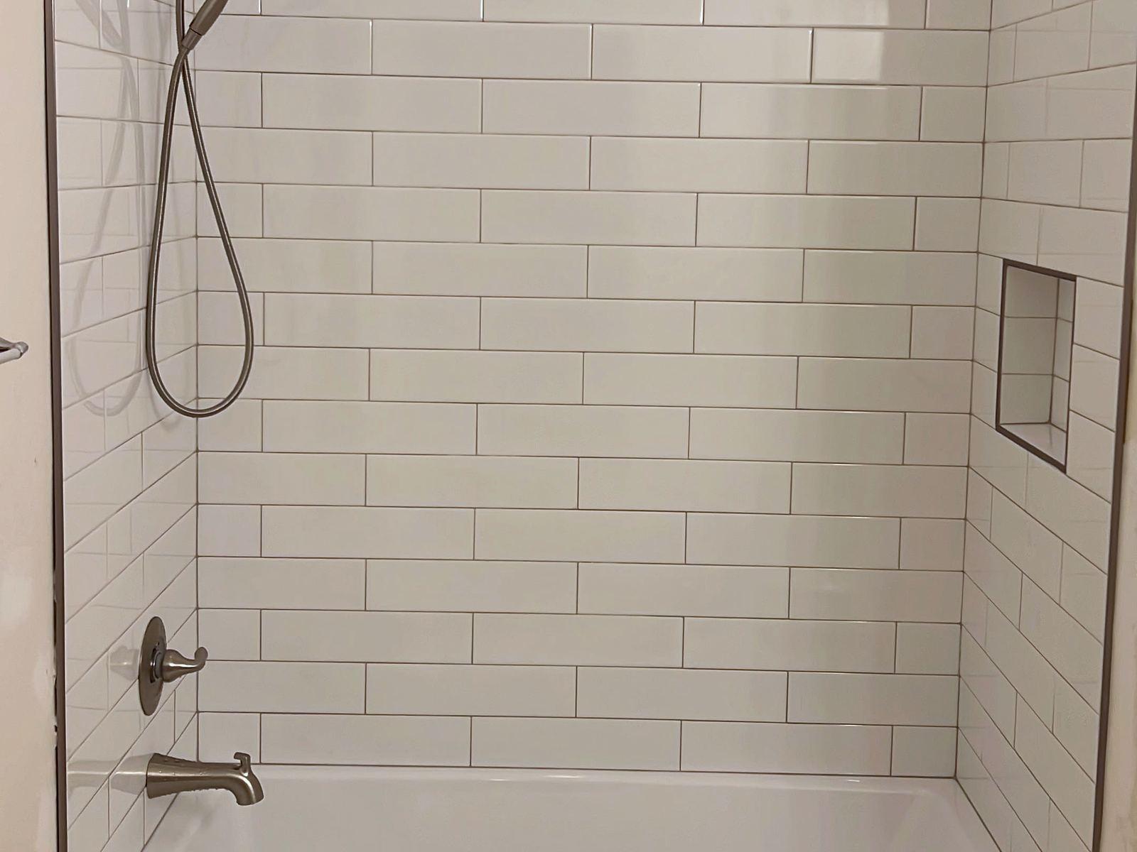 Newly tiled tub surround in white subway tile with a built-in niche